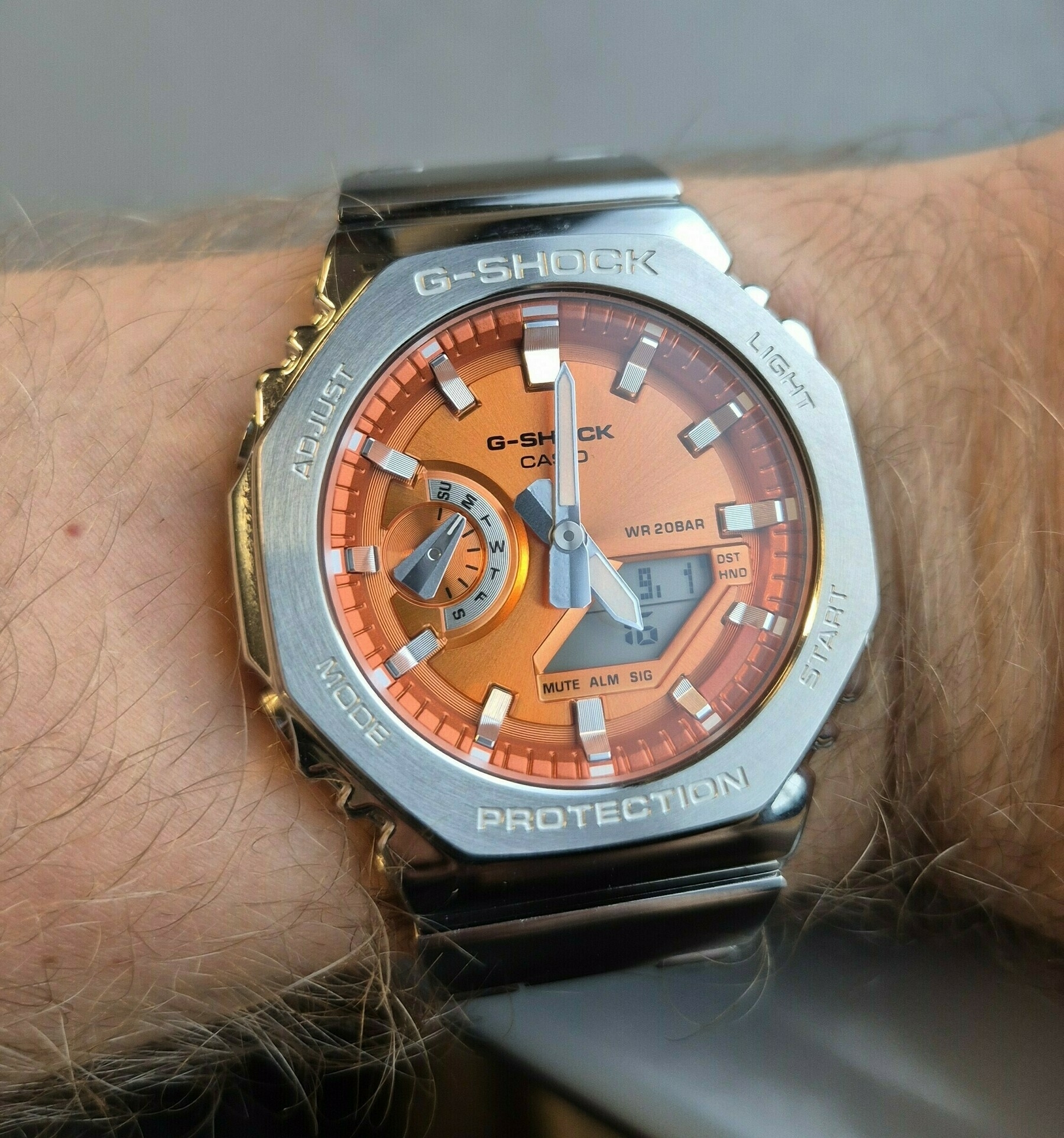 Auto-generated description: A person is wearing a Casio G-Shock wristwatch with a vibrant orange face and a metal bezel.